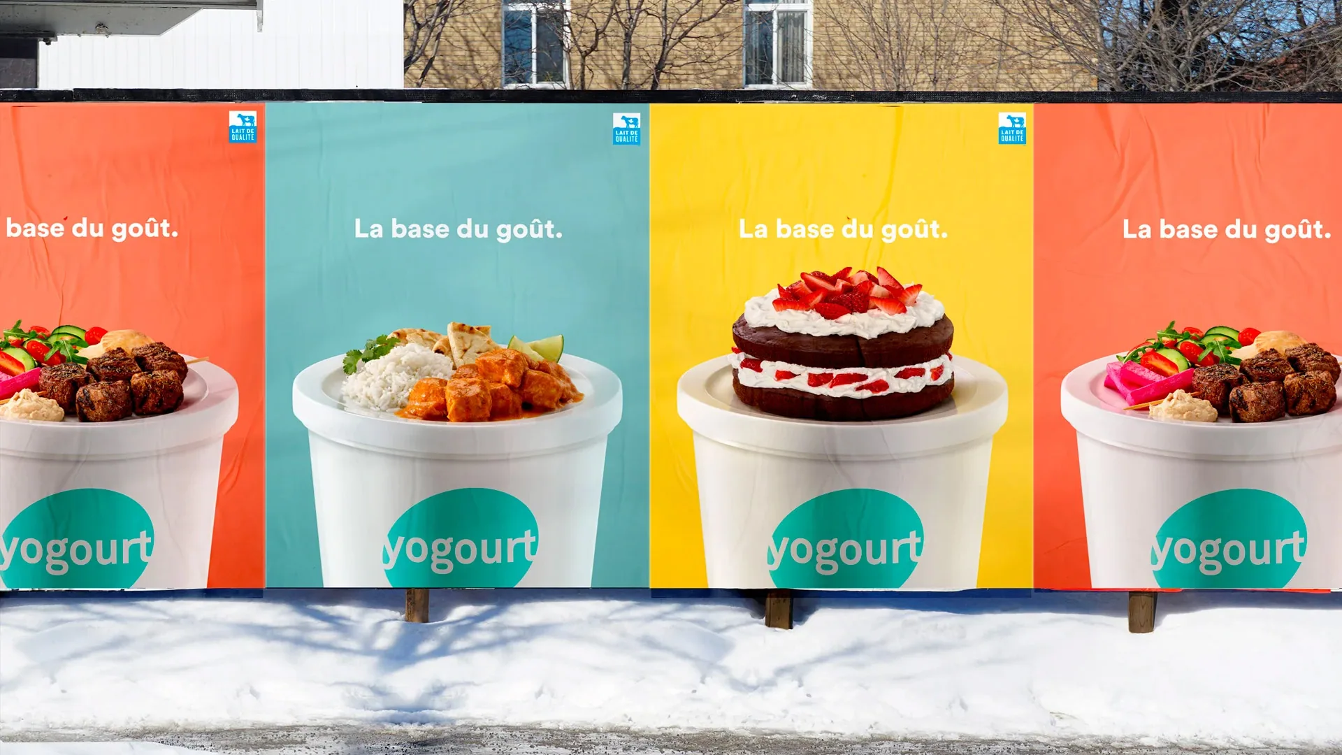 Row of “La base du goût” posters on a snowy construction fence, each with a dish in a yogourt cup